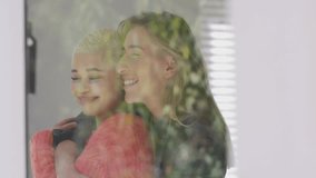 Two women leaning behind glass, interacting with floating thumbs-up and heart icons for marketing. Friends, social media, interaction, contemporary, vibrant, communication, lifestyle - Powered by Shutterstock - Get 15% off with code: PIKWIZARD15