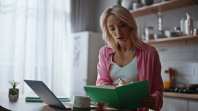 Smart girl freelancer making notes in notepad looking laptop screen at kitchen closeup. Thoughtful woman working computer sitting cozy modern kitchen. Focused businesswoman watching online webinar - Powered by Shutterstock - Get 15% off with code: PIKWIZARD15