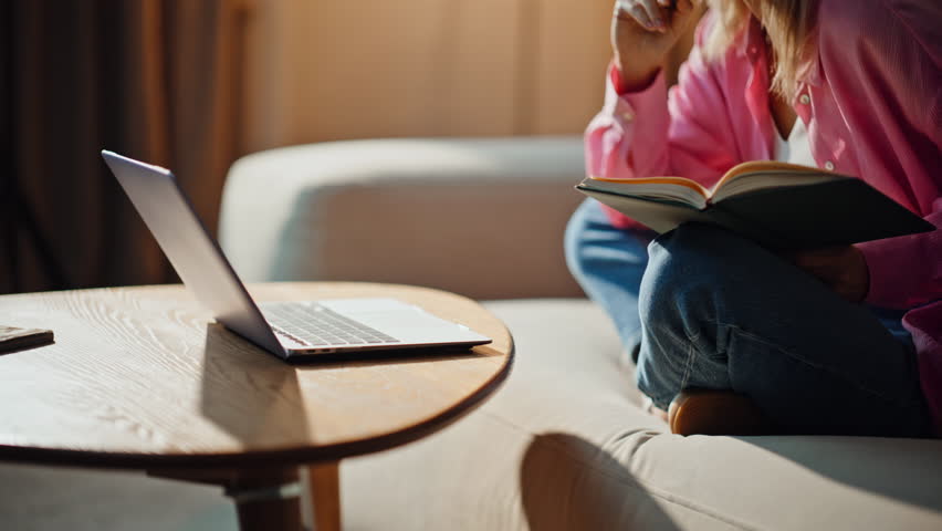 Online student pressing laptop button studying at home couch closeup. Serious woman making notes in copybook listening virtual webinar. Relaxed girl watching educational video on sofa with notebook