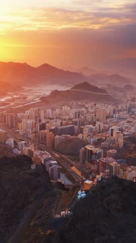 A breathtaking aerial view of Mecca city at sunrise, showing urban architecture surrounded by majestic mountains under a golden sky