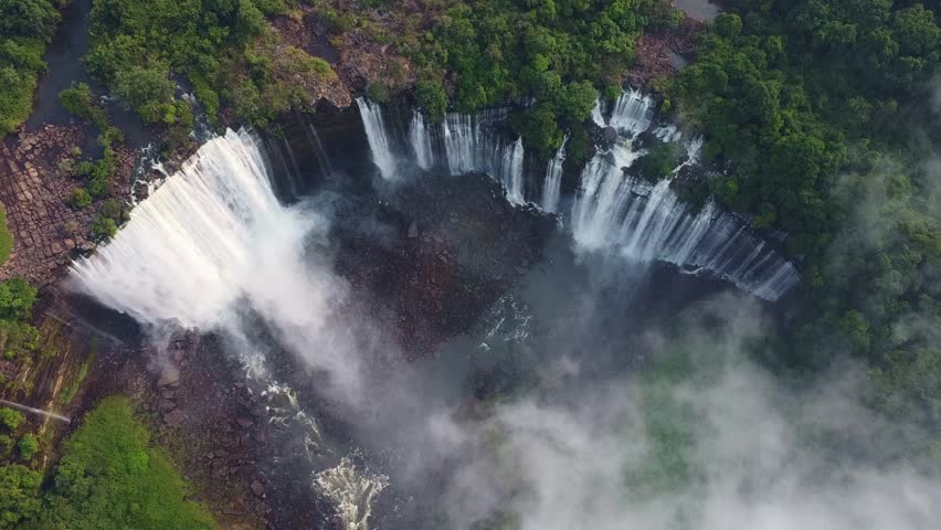 a beautiful aerial view of a waterfall cascading down a cliff surrounded by lush green vegetation. Angola