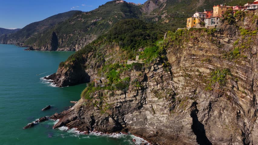 Colorful cliffside homes above Corniglia’s rocky coast on a sunny day in Cinque Terre