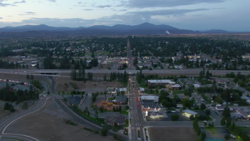 Aerial Backward Beautiful Shot Of Residential Town By Mountains Under Clouds At Dusk - Post Falls, Idaho
