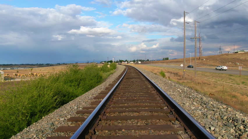Aerial: Scenic Shot Of Cars Moving On Roads Under Clouds, Drone Flying Forward Over Railroad Tracks During Sunny Day - Post Falls, Idaho