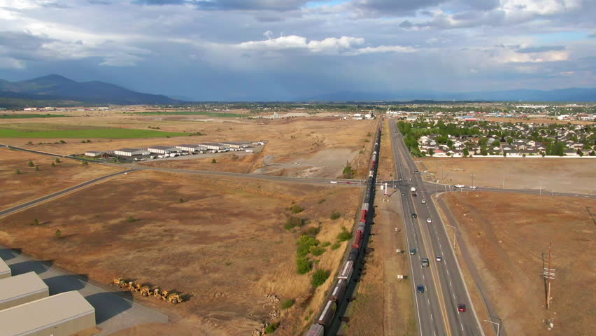 Aerial Descending Scenic View Of Railway By Cars Moving On Road, Drone Flying Backwards During Sunny Day - Post Falls, Idaho