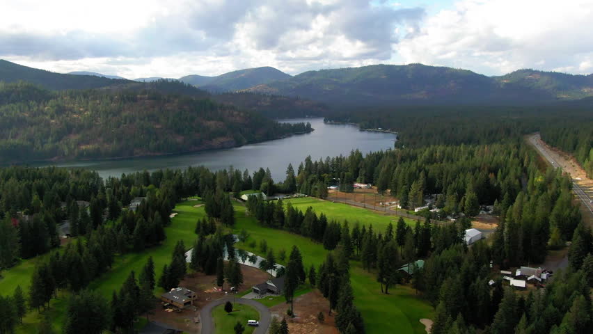 Aerial Panning Scenic View Of Rippled Lake Amidst Green Trees, Drone Flying Over Hills Under Cloudy Sky - Rathdrum, Idaho