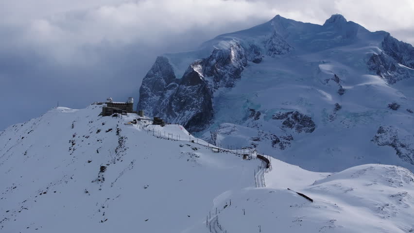 Aerial Panning Shot Of Observatory On Snowcapped Mountain With Train Against Cloudy Sky - Zermatt, Switzerland