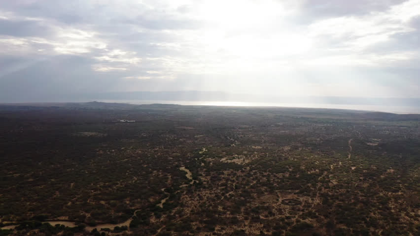 Aerial shot capturing the vast, undulating terrain of a dry, sparsely vegetated landscape under overcast skies.
