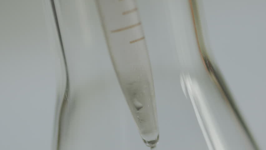 Detailed close-up of a liquid pouring from a measuring cylinder into a flask in a laboratory setting.