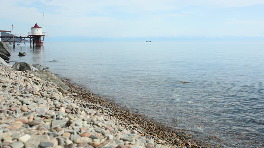 The shore of Lake Baikal near the village of Listvyanka on a summer evening. Pebble beach, small waves in the lake 