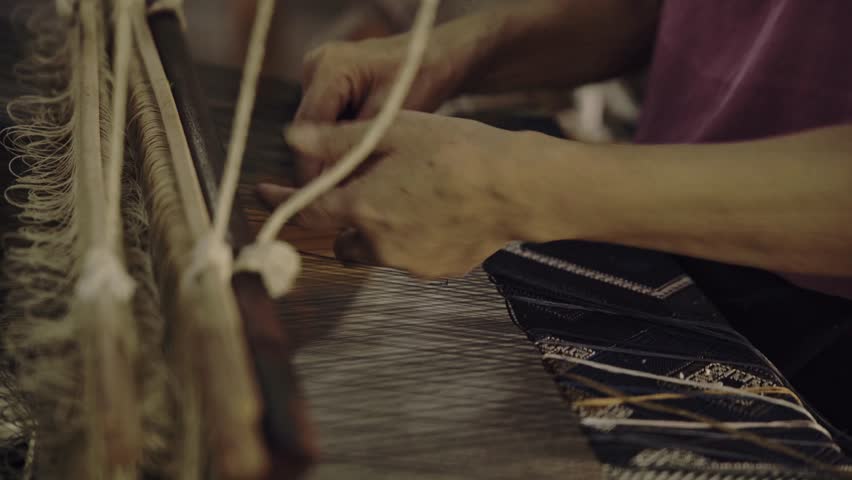 A Laos woman skillfully weaves on a traditional loom, creating intricate patterns with vibrant threads, preserving the rich textile heritage of her culture. 4k video footage
