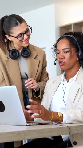 Two customer service representatives collaborate, using a laptop and headsets, providing assistance and solutions