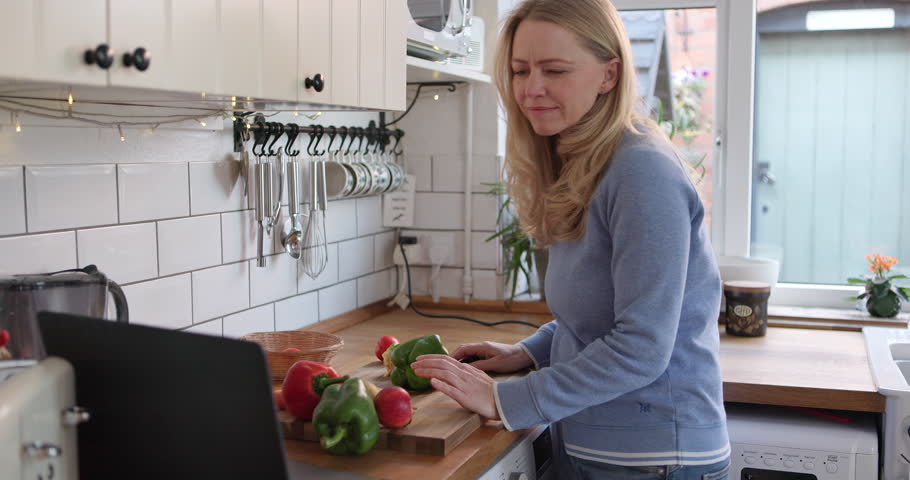 Woman, reading on tablet and cooking in kitchen with recipe or woman to cut vegetables with knife on board for healthy dinner. Mobile app, instructions and meal with nutrition or online diet plan