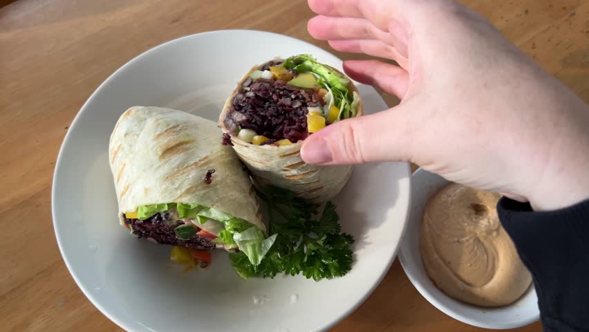burrito in pita bread with beans Female hand holding burrito and covering above yellow plastic basket. Close-up of woman holding vegetarian burrito with sauce. Traditional Mexican cuisine