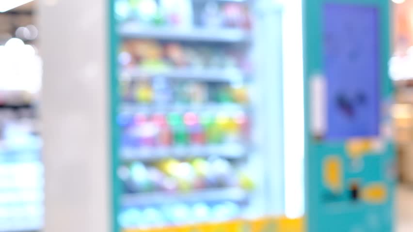 A blurry image of a vending machine with a blue and white color scheme. The machine is filled with various drinks and snacks