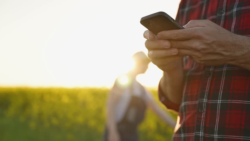 Smart farming, using smartphone app on canola rapeseed plantation field, portrait of two farmers, male and female, working in field, 4K with selective focus