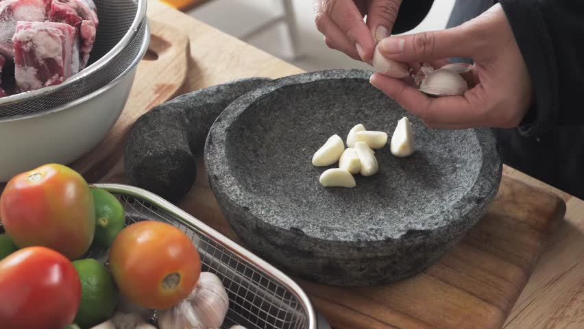 A woman is peeling garlic by hand, which will later be crushed using a mortar and pestle