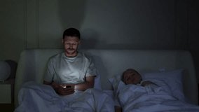 Stressed man engrossed in smartphone at night, disturbing wife sleep in bed. Male struggle with insomnia, phone digital addiction, endless scrolling through social media, sleep disruption, nomophobia - Powered by Shutterstock - Get 15% off with code: PIKWIZARD15