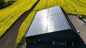 Aerial footage of large solar panel system on the roof of a modern agricultural barn, surrounded by yellow rapeseed fields in spring. Farm equipment storage with large solar photovoltaic  array.  - Powered by Shutterstock - Get 15% off with code: PIKWIZARD15
