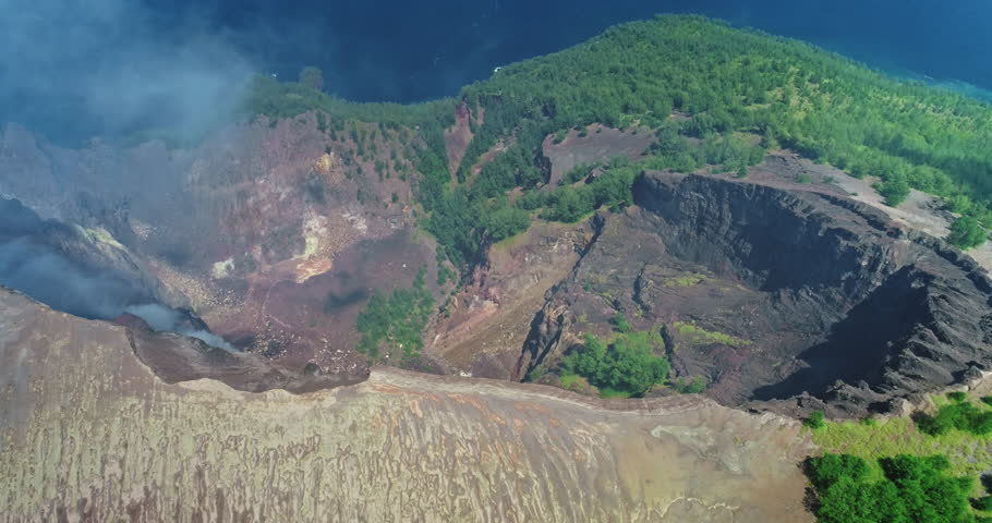 Volcanic fumes are rising from inside the crater of Mount Kelimutu in Flores, Indonesia, surrounded by lush vegetation, showing the raw power of nature