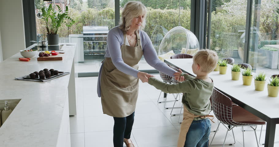 Kitchen, dance or happy grandma with a child playing or laughing with joy in family home together. Fun grandmother, kid baking or old woman dancing, holding hands or bonding in retirement or house