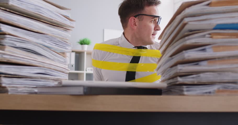 Bookkeeper escaping from workplace. Funny man who has become office slave, fastened to chair with scotch tape, sitting by desk with paperwork, cautiously looks around and starts stealthy movement out