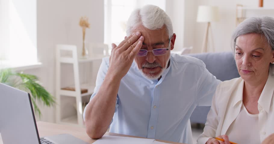 Married senior couple with money problems having argument over family budget. Elderly mature man and woman having disagreement while paying domestic bills and calculating expenditures.
