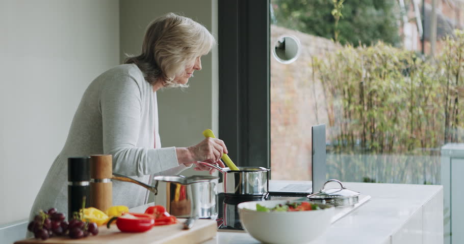 Elderly woman, cooking and tasting food with chef skill, laptop with online recipe and prepare meal in kitchen. Retirement, nutrition and female person season to taste, process instructions on blog