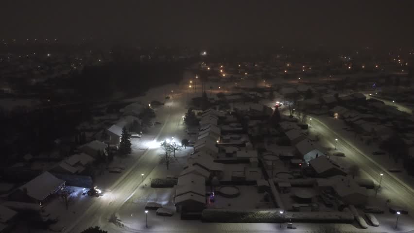 Aerial View Of Snow-covered Neighborhood At Night With Snowblower Tractor At Work. Saint-Constant, Quebec, Canada. sideways shot