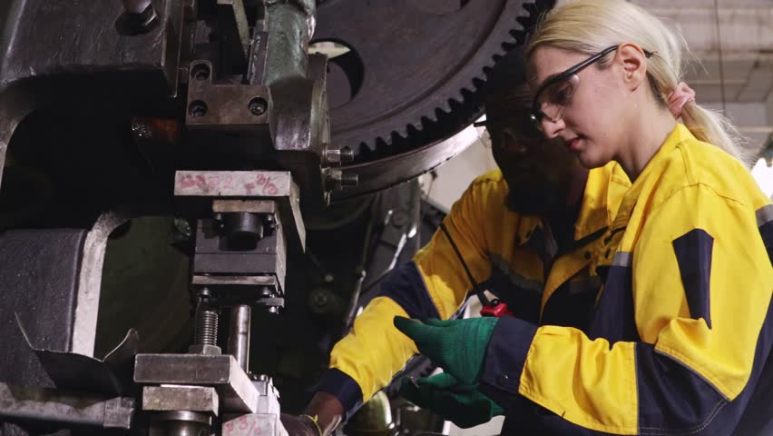 Two male and female factory mechanics operate metal stamping machines together in a factory in the automotive parts manufacturing industry, turning and metal stamping.