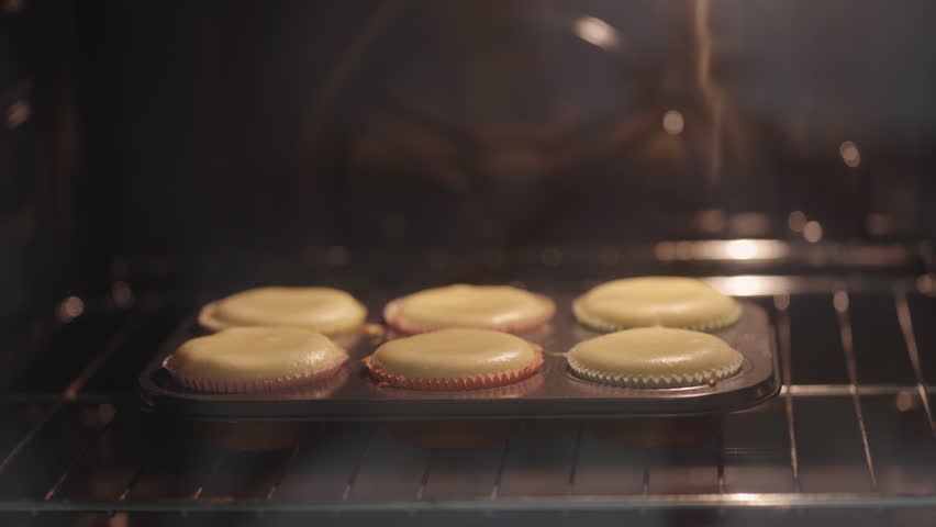 Timelapse of cupcakes muffins baking and rising in muffin tin inside an electric oven. Closeup shot showcasing homemade bakery and pastry in cooking process 