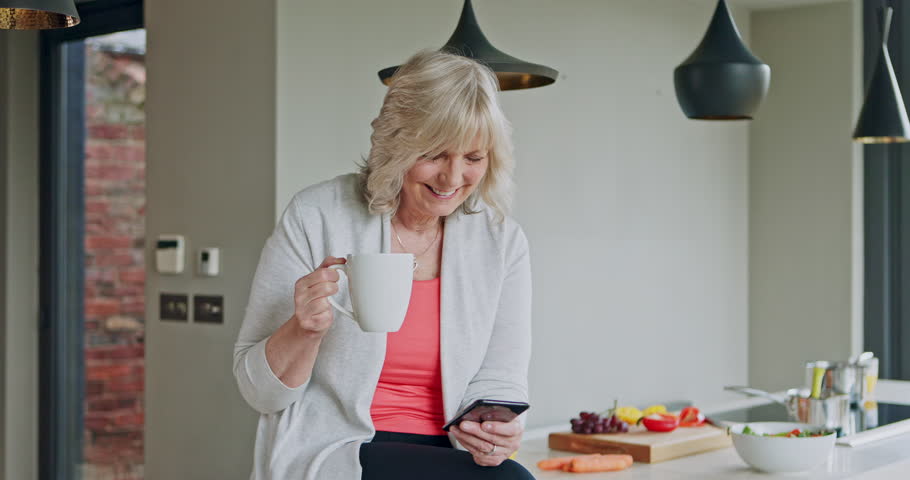 Home, phone and coffee, mature woman laughing at meme, online news on mobile app or social media in kitchen. Drink, cup and breakfast, model networking on cellphone in home to relax in retirement.