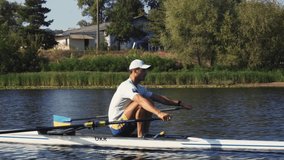 Rower solo training. Side view of young caucasian male rower, during a rowing practice, athlete sitting in a boat in the river Dnipro, rows through a calm water in autumn. 4k footage. Caucasian man tr - Powered by Shutterstock - Get 15% off with code: PIKWIZARD15