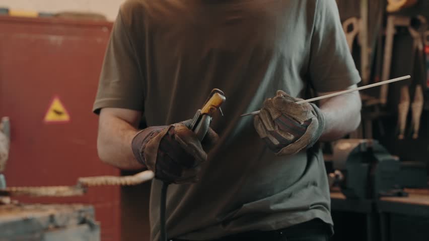 Man holding welding rod with gloves preparing for metalwork indoors - slow motion
