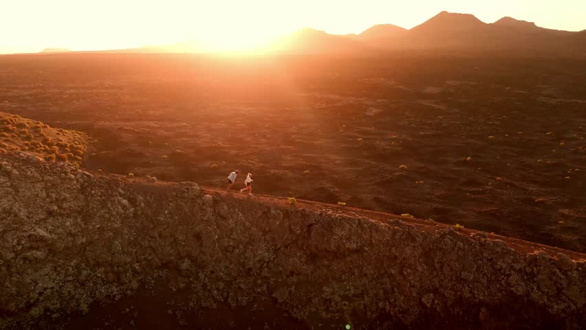 A romantic aerial drone shot of a couple walking together at sunset along the rim of Volcano del Cuervo in Lanzarote, Canary Islands, Spain.