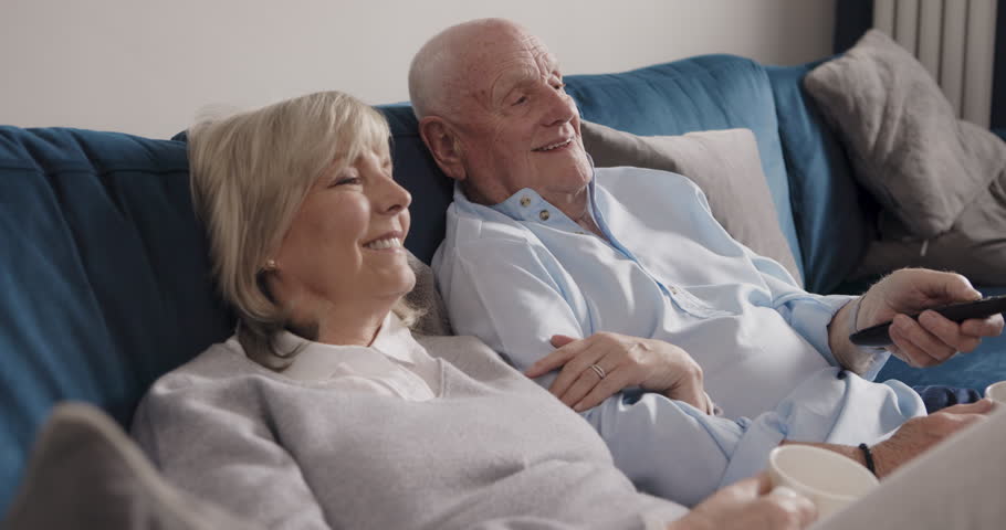 Relax, laugh and happy elderly couple watching tv, funny subscription video or streaming home media channel. Remote control, quality bonding time and senior people laughing with television program
