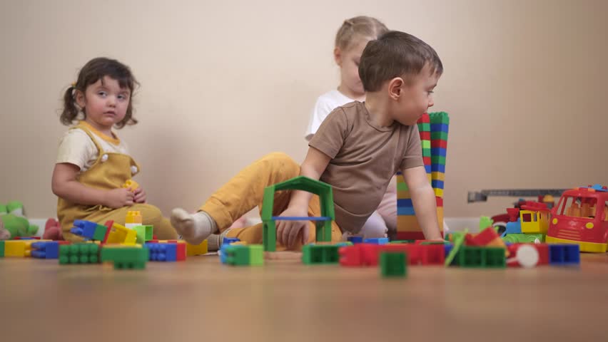 Three children playing with blocks. Children play together in a group. Lifestyle build a new floor for your kindergarten with toys and a constructor. Three kids engaging with building blocks.
