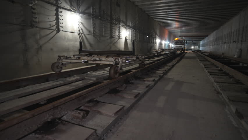 Construction cart rolls smoothly along metro rails deep in metro zone. Wheels clatter quietly in dark tunnel. Cart used to deliver materials
