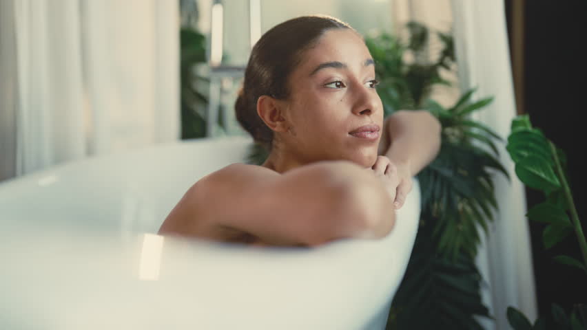 Feel loneliness, sad lady lying in bathtub in her modern bathroom, portrait. Single lady spending weekend at home, time for herself and beauty treatments, enjoy solitude, dreaming mixed race woman