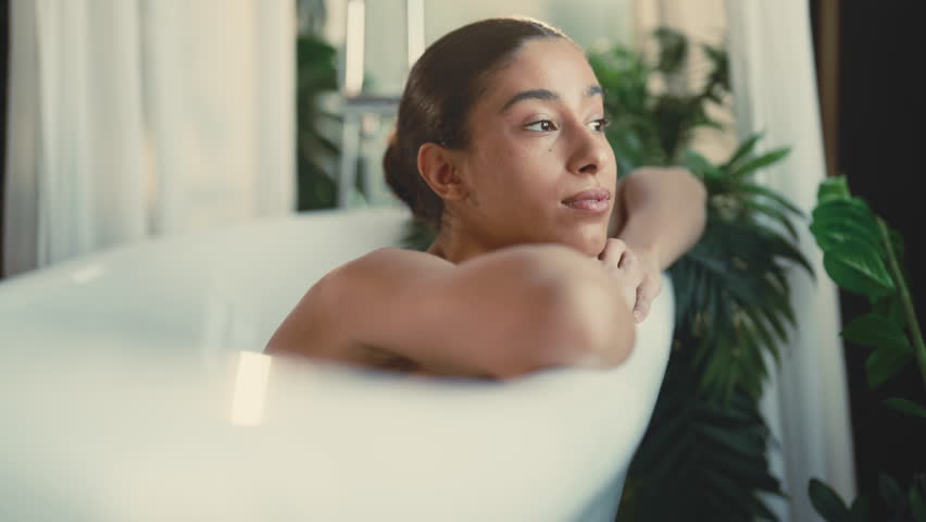 Feel loneliness, sad lady lying in bathtub in her modern bathroom, portrait. Single lady spending weekend at home, time for herself and beauty treatments, enjoy solitude, dreaming mixed race woman