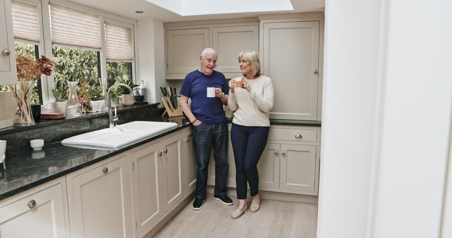 Happy, relax and senior couple drinking coffee, talking and bonding in the kitchen in the morning. Laughing, calm and an elderly man and woman speaking with a cup of tea together in their home