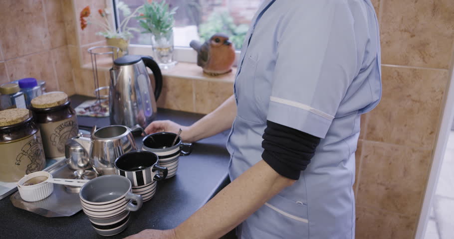 Kitchen, caregiver or nurse waiting for kettle for tea in cup at nursing home or rehabilitation center at breakfast time. Healthcare, support and elderly woman working in senior care making coffee.