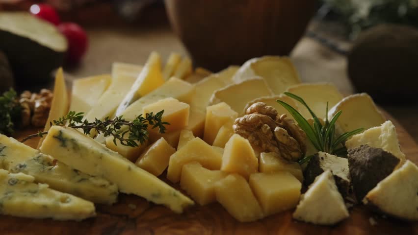 Close-up still life of cheese and meat delicacies. Craft cheeses and cold meat are on the table among aromatic rosemary, cherry tomatoes and other snacks. Gourmet plate antipasto setting. Cheese board