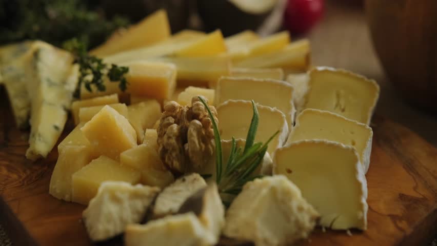 Close-up still life of cheese and meat delicacies. Craft cheeses and cold meat are on the table among aromatic rosemary, cherry tomatoes and other snacks. Gourmet plate antipasto setting. Cheese board
