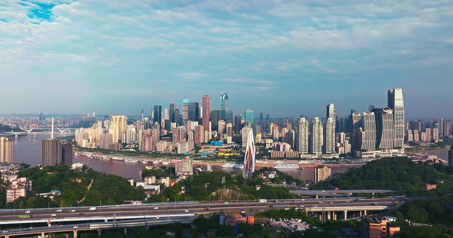 Aerial shot of the dense modern cityscape featuring skyscrapers, a prominent bridge, and river winding through the hilly terrain in Chongqing, China.