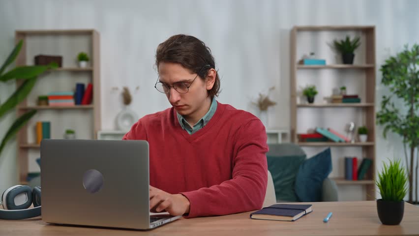 Daily lifestyle concept. Young adult man spending time at home, man student sits at desk works on computer, finishing studying closing laptop, sighing and dancing happy dance. Slow motion.