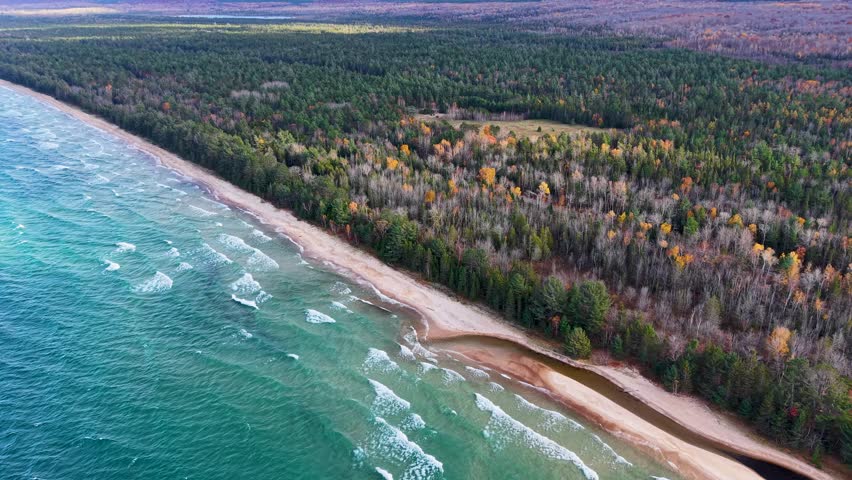 Stunning aerial drone footage of Lake Superior’s coastline featuring gentle waves, sandy beach, and vibrant fall foliage in Michigan’s Upper Peninsula