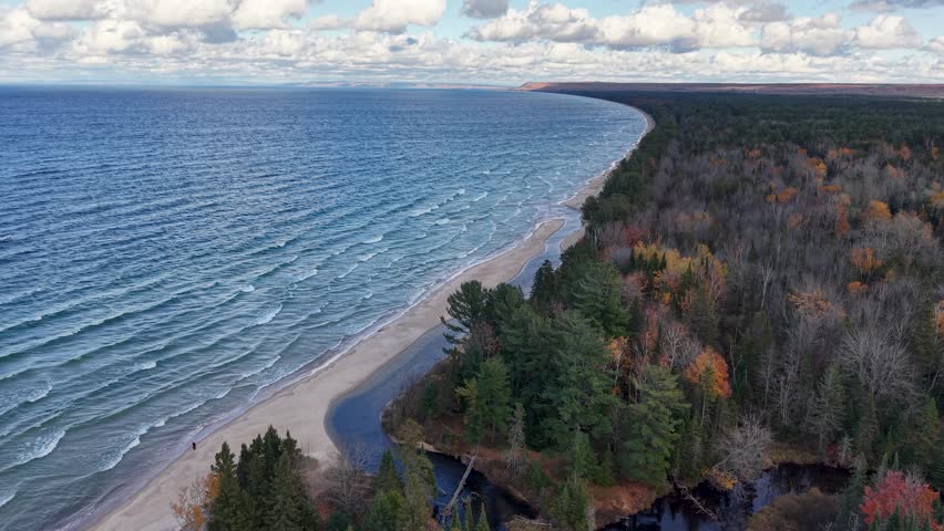 Dramatic drone shot of Lake Superior shoreline with autumn trees and rippling waves in Michigan’s Upper Peninsula