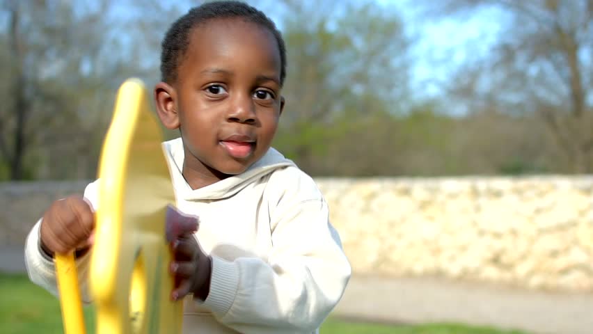 Cute black child playing on a merry go round in a park