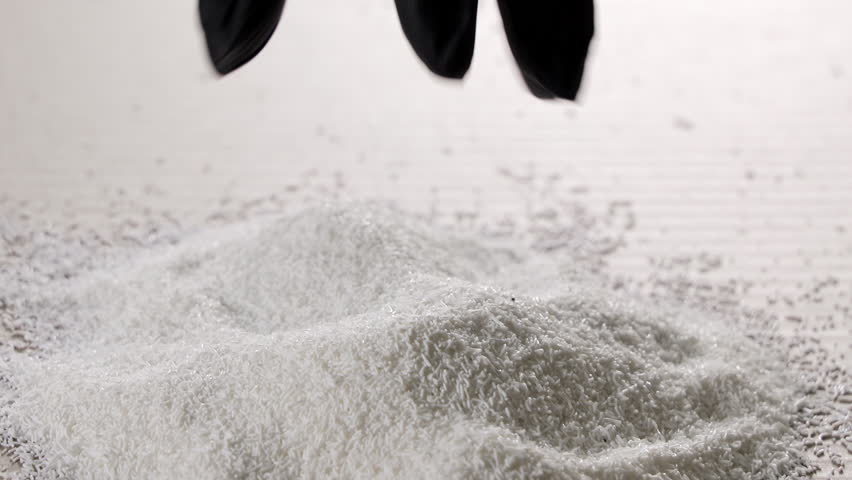 Black gloved hand pouring fine white granules, clean synthetic material flowing down